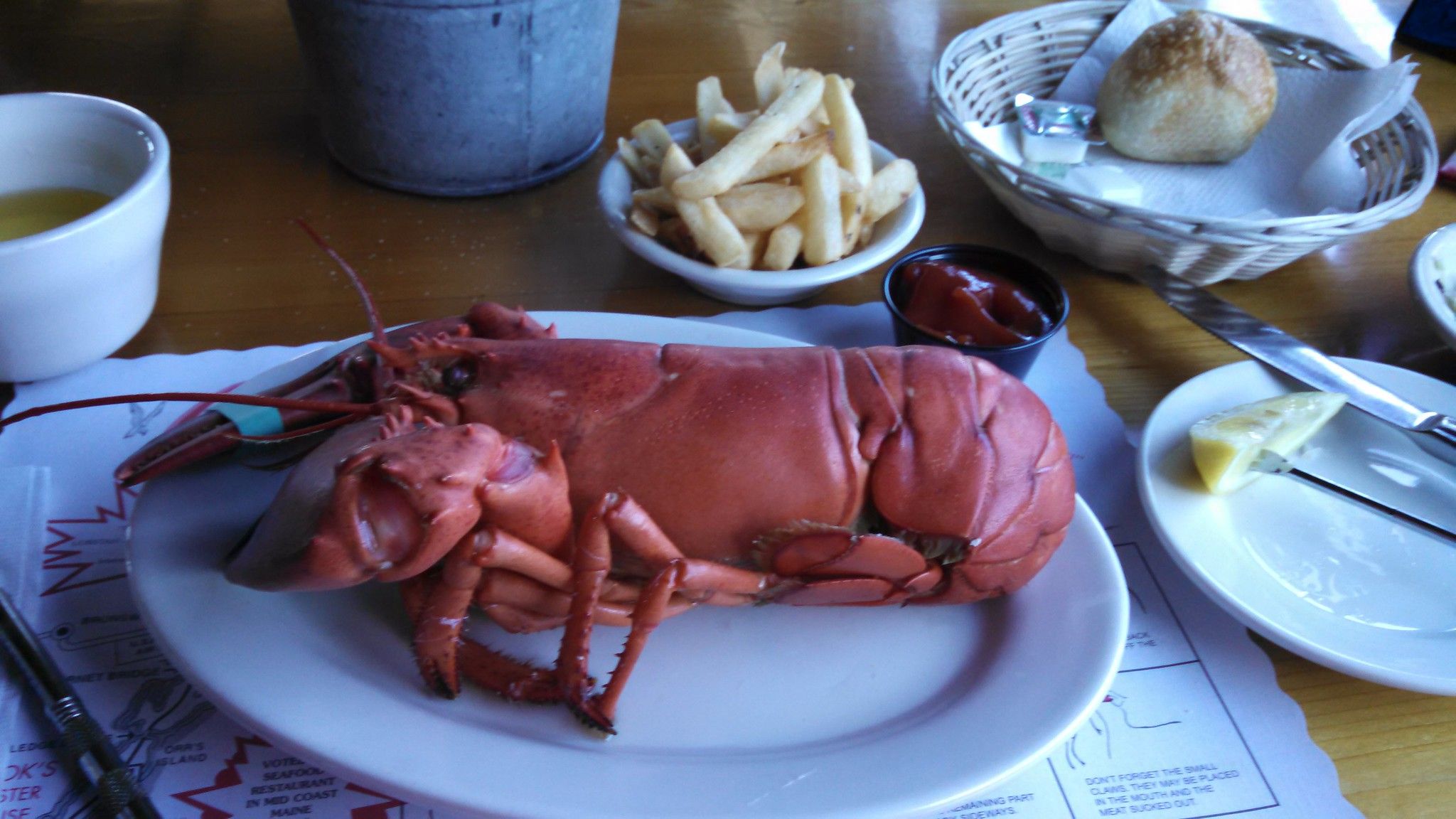 A lobster on a plate on a table and some fries in a restaurant.